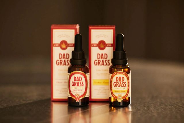 Two Dad Grass CBD tincture dropper bottles with red and gold labels beside their matching product boxes.